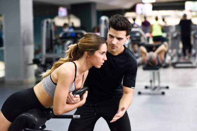 Eine Frau trainiert im Fitness. Daneben steht der Trainer und motiviert sie.